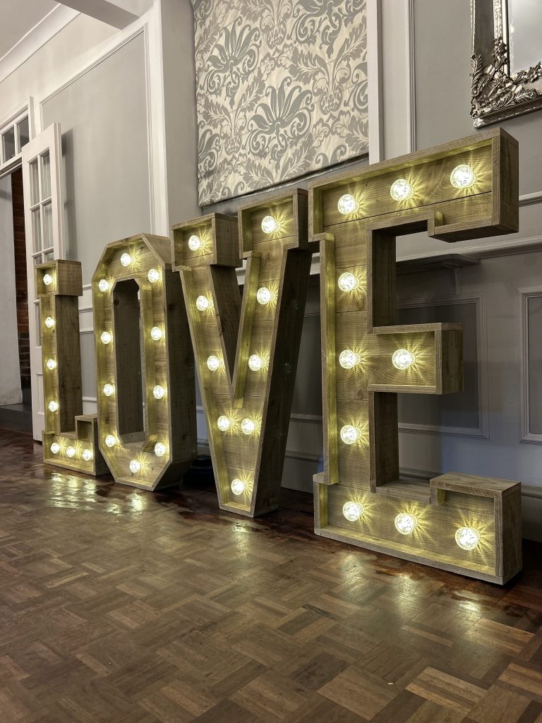LOVE Letters – From £175 Our 4ft ‘LOVE’ letters are the essence of romance turned into a radiant spectacle. Each letter stands tall, casting a soft, inviting glow that harmonises with the joyful celebration of your union. These aren’t just letters; they are the beacons of your love story, meticulously designed with bright, energy-efficient LED bulbs that offer an enchanting luminescence to your venue. Whether nestled by the dance floor, welcoming guests at the entrance, or serving as an exquisite photo backdrop, our ‘LOVE’ letters are more than decor—they are a memorable experience. Their timeless design complements any wedding theme, from the ultra-modern to the whimsically vintage, transforming your space into a storybook setting. Mr & Mrs Letters – From £225 Celebrate the beginning of your forever with our ‘Mr & Mrs’ letters, a testament to your newly shared surname. These 4ft symbols of commitment and togetherness are not only an elegant decorative element but also a tribute to the journey you embark upon as life partners. Each character glows with the promise of future happiness, standing as a proud announcement of your marital bond. The letters’ soft lighting adds an air of sophistication to your reception, inviting guests to revel in the essence of your wedding day. Designed with versatility in mind, they adapt seamlessly to any setting, providing a focal point that is both visually stunning and deeply personal. These letters don’t just spell out a title; they encapsulate the essence of the wedding celebration—unity, love, and a touch of grandeur.